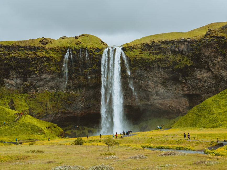 Explore Seljalandsfoss, a stunning Icelandic waterfall surrounded by lush green cliffs and scenic views, with visitors admiring the beauty.
