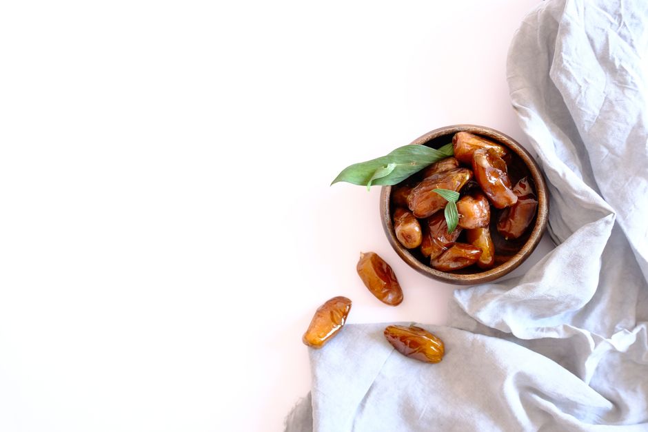 A bowl of dates with leaves on a white background, capturing a Ramadan theme.