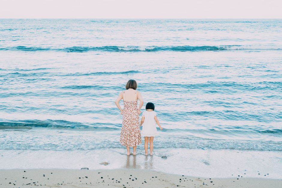 A serene moment of a mother and daughter standing at the beach, enjoying the ocean view.