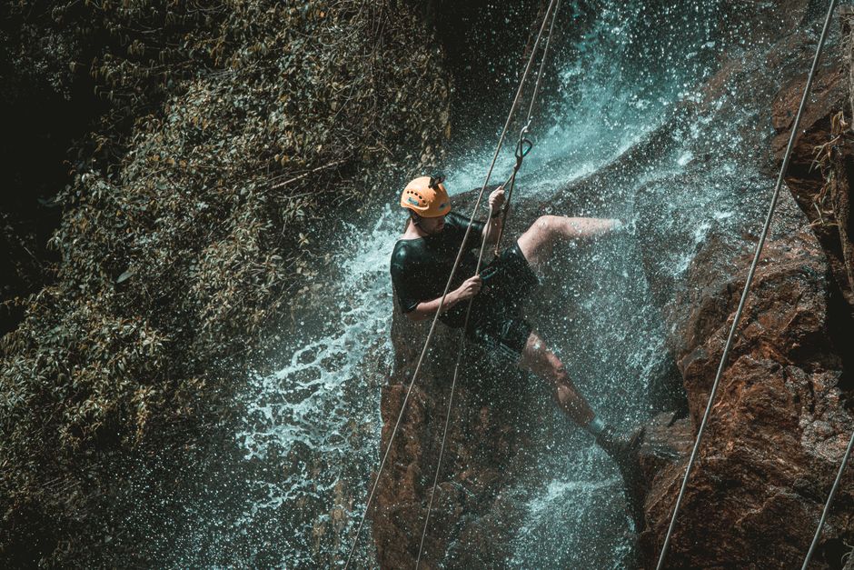 An adventurous person rappelling down a waterfall in a natural setting, showcasing outdoor excitement.