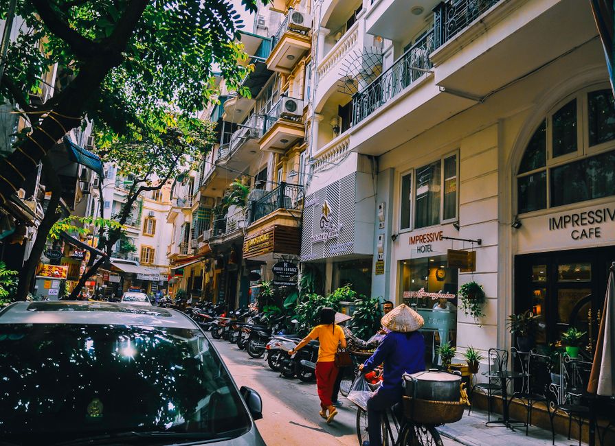 Vibrant street life in Hanoi with locals, cafes, and motorbikes on a sunny day.