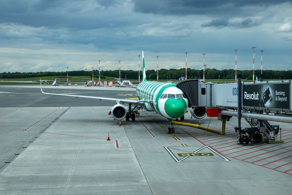 Green and white Airbus A320 parked at a gate in Hamburg Airport on a cloudy day.