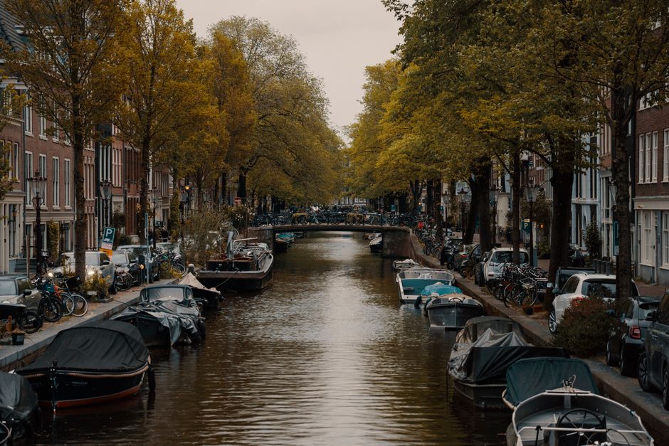 Picturesque Amsterdam canal with boats and autumn trees lining the streets.