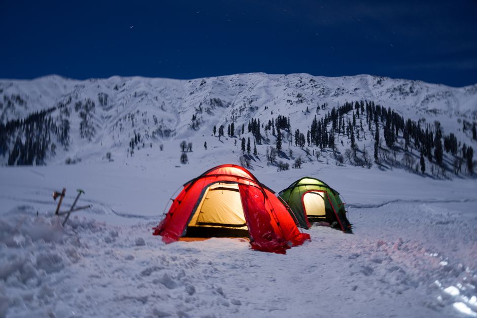 Snow-covered campsite with tents under a starry night sky, perfect for winter adventure.