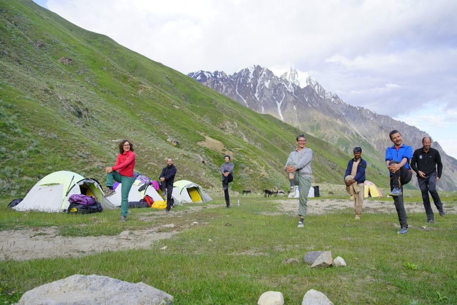 A group of adults stretching at a campsite with tents and mountains in the background.