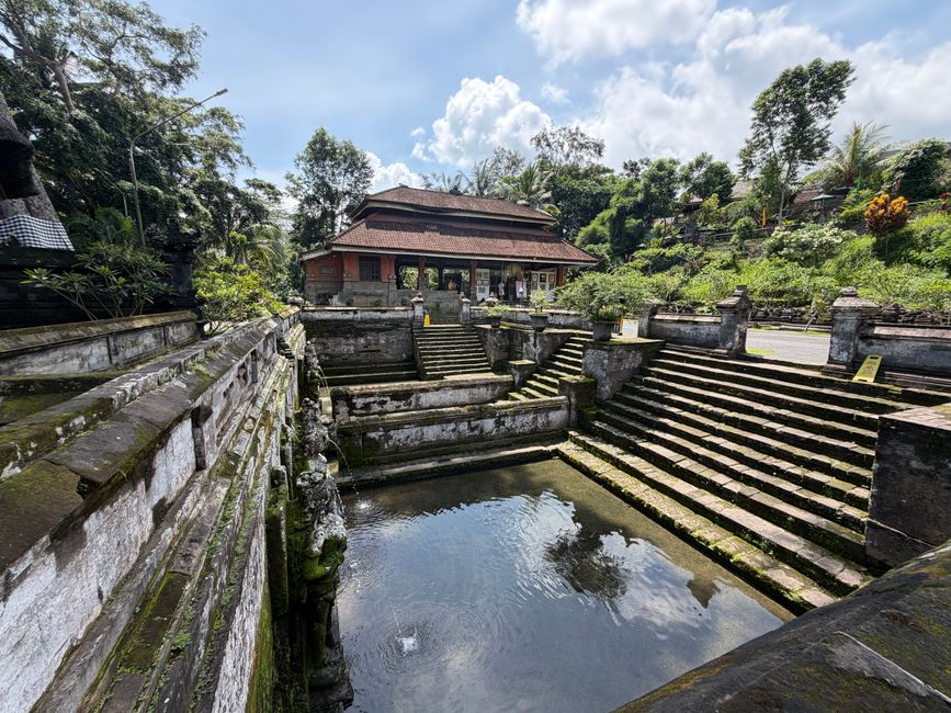 Serene temple with stone steps reflected in Bali's sacred water under a bright sky.