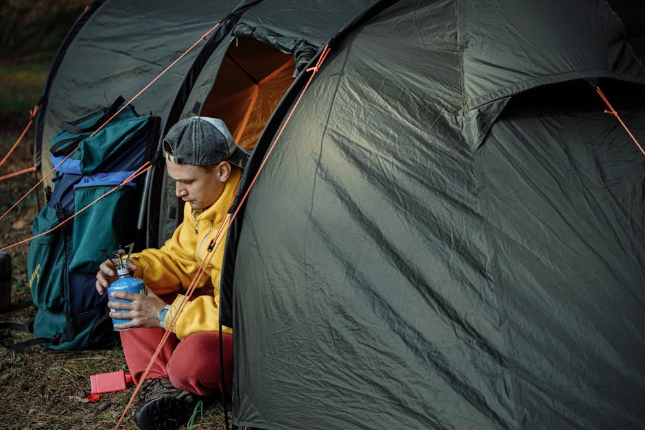 A camper sets up a gas burner outside a tent in a forest campsite.