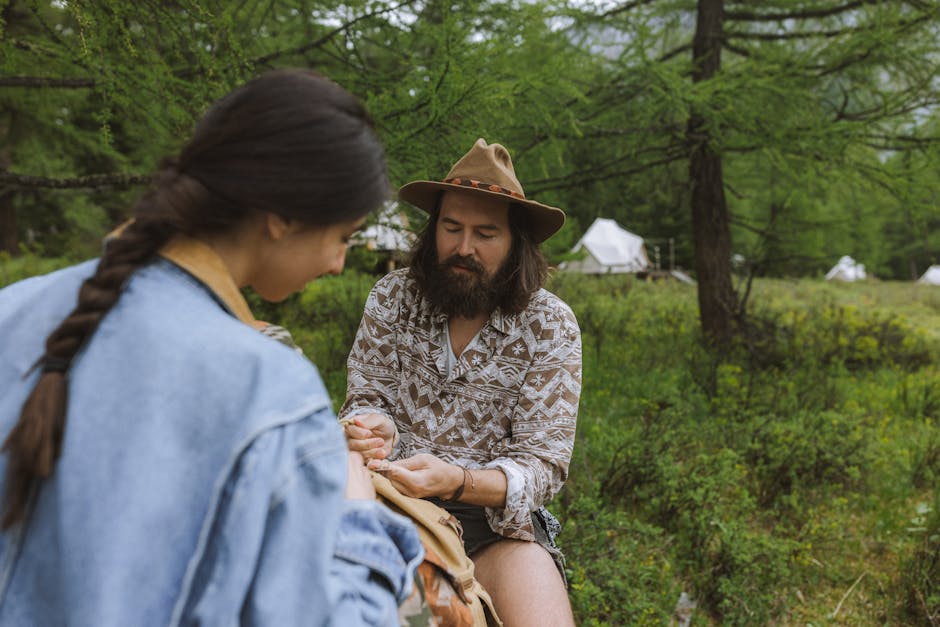 A couple enjoys quality time in a scenic forest setting with tents in the background, highlighting a love for nature and adventure.