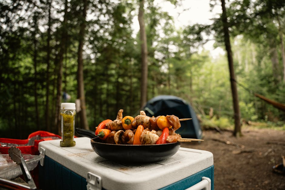 Grilled skewers on a cooler by a tent in the forest, perfect for camping vibes.