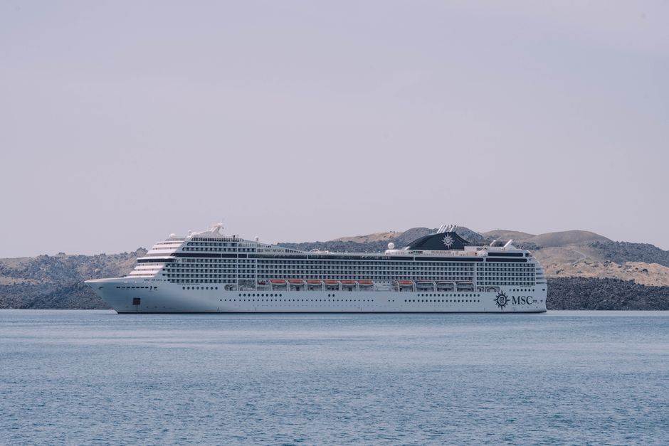 White MSC cruise ship sailing peacefully on the sea against a scenic coastline backdrop.