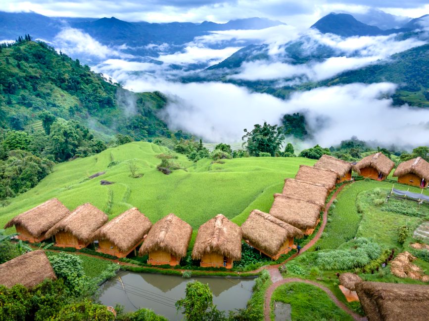 Picturesque aerial view of lush rice terraces and traditional nipa huts in a mountainous rural landscape.