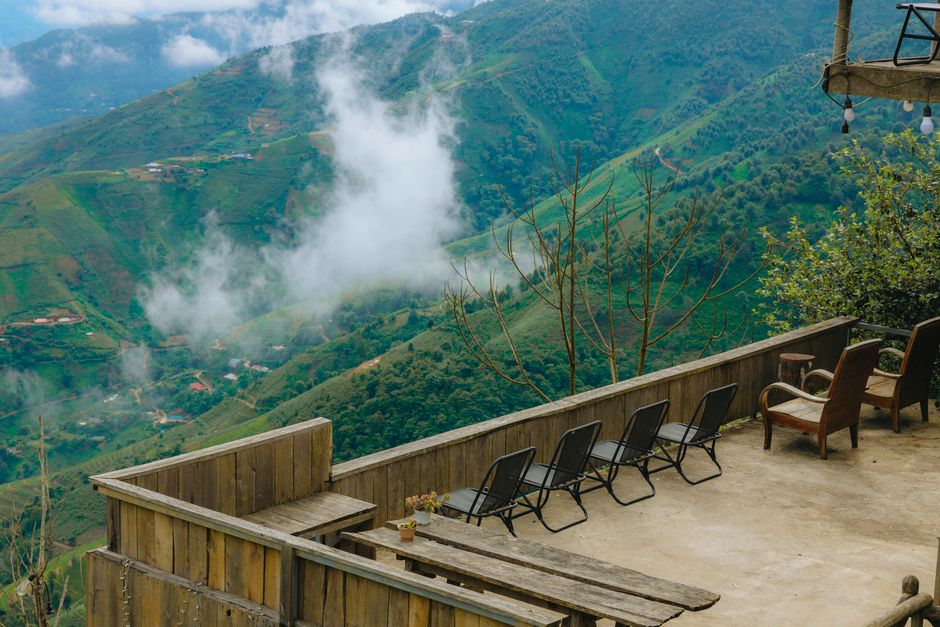 Tranquil mountain view from a rustic terrace with empty chairs and tables, perfect for relaxation.