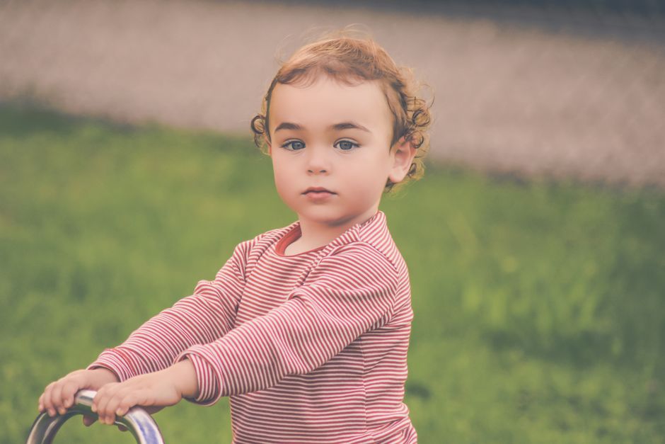 Adorable young child with curly hair playing outdoors in a striped shirt, enjoying a sunny day.