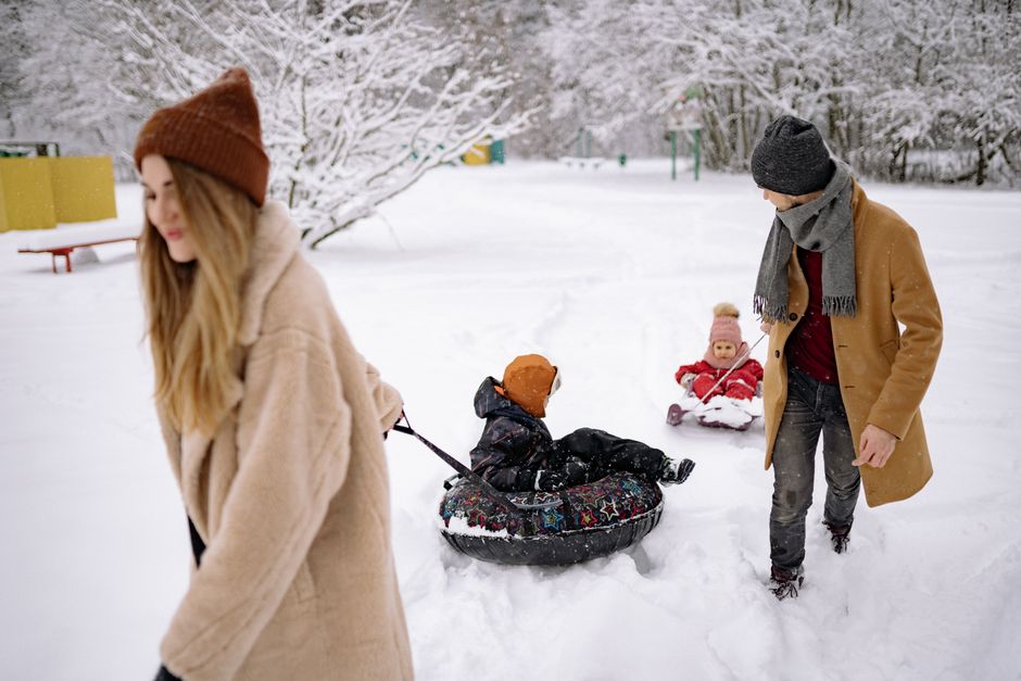 Family enjoying a playful day in the snow with tubing activities, dressed in warm winter clothing.