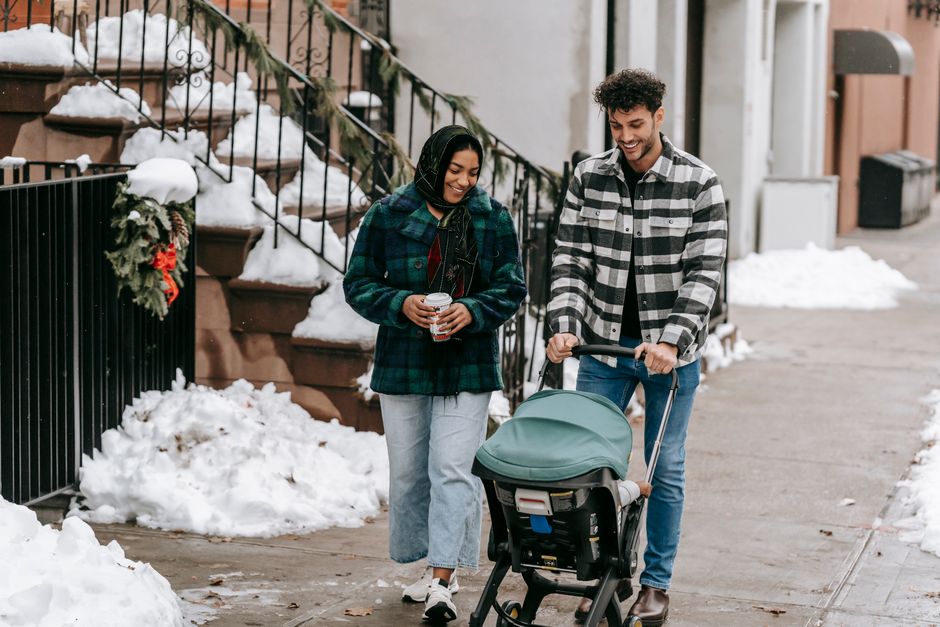 Full body of ethnic couple wearing casual clothes walking along sidewalk with stroller on