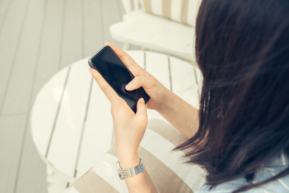 Woman using a smartphone while sitting outdoors on a sunny day.