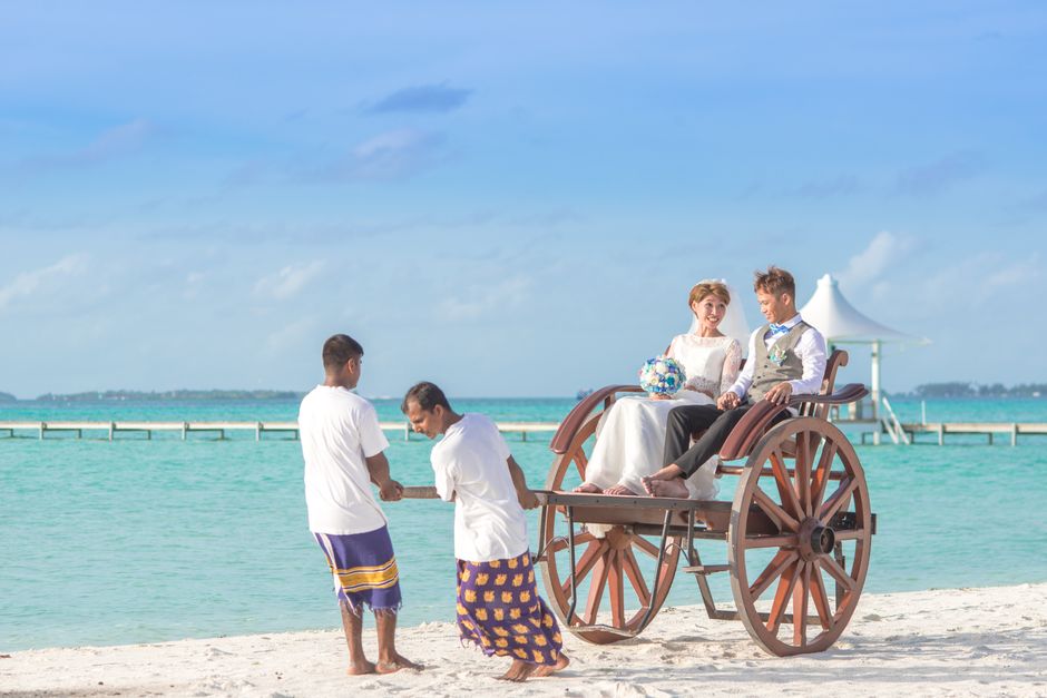 A joyful couple enjoys a cart ride on a scenic tropical beach, perfect for romantic getaway visuals.