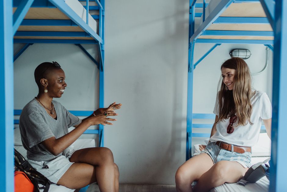 Two women enjoying a friendly conversation in a hostel room with blue bunk beds.