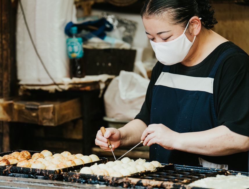 A Japanese street food vendor skillfully prepares takoyaki at an outdoor market.