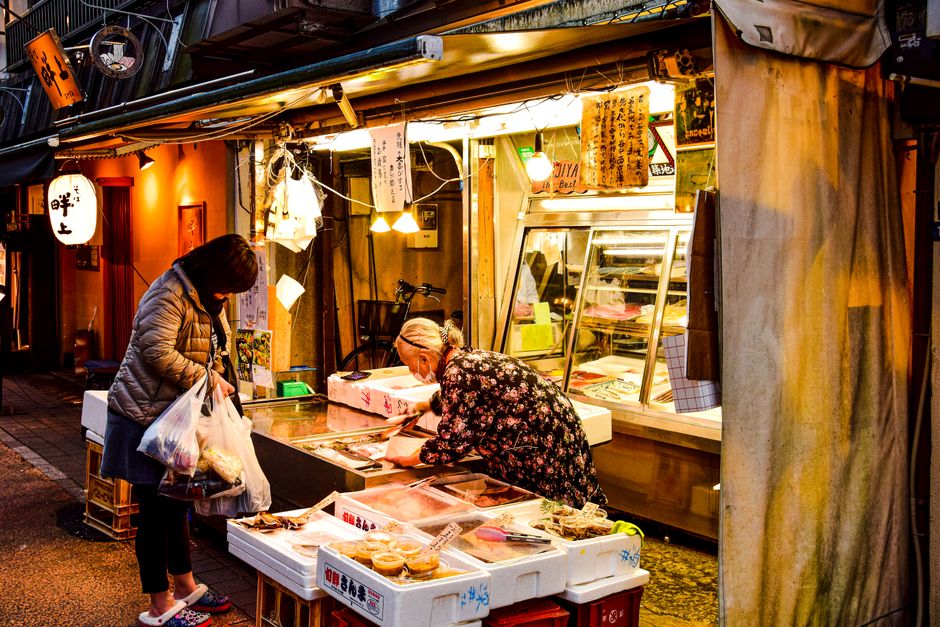 A bustling street market at night with women shopping for groceries under illuminated stalls.