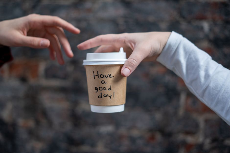 Close-up shot of a disposable coffee cup with 'Have a good day!' message being passed between two hands.