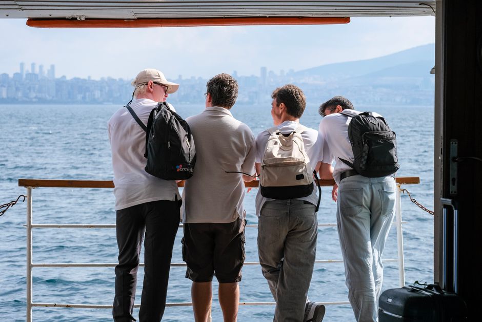 Four men on a ferry deck, gazing at a scenic waterfront city skyline.