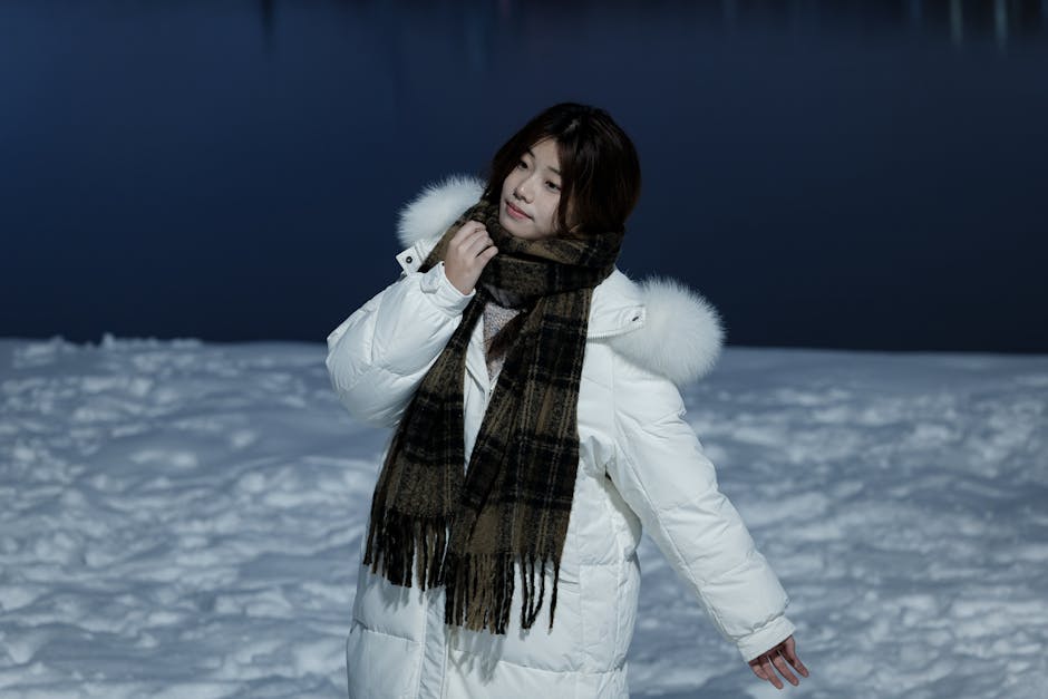 Woman in a white jacket and scarf poses gracefully on snowy landscape at night.