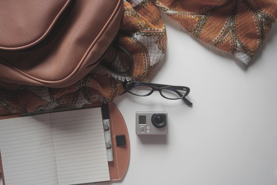 A stylish arrangement of travel essentials including a camera, notebook, eyeglasses, and accessories on a white background.