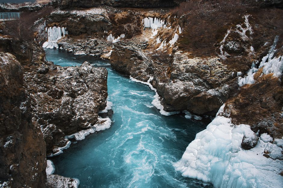 Captivating winter scene of an icy river with vivid blue waters meandering through a rocky gorge in Iceland.