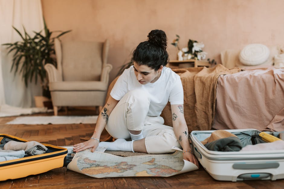 Woman sitting on floor packing suitcases with map, preparing for travel.