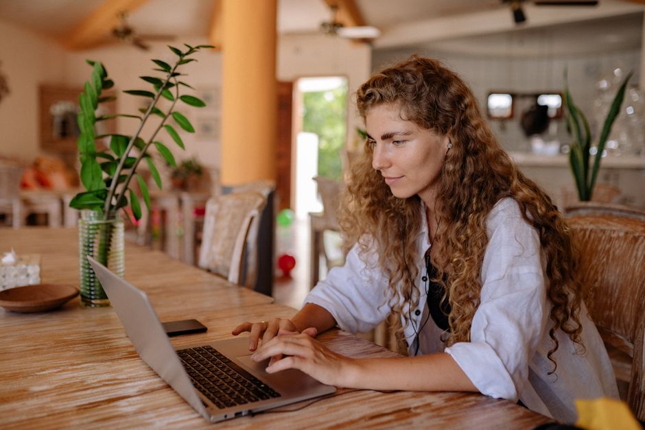 Young woman with curly hair working on a laptop indoors, focused and productive.