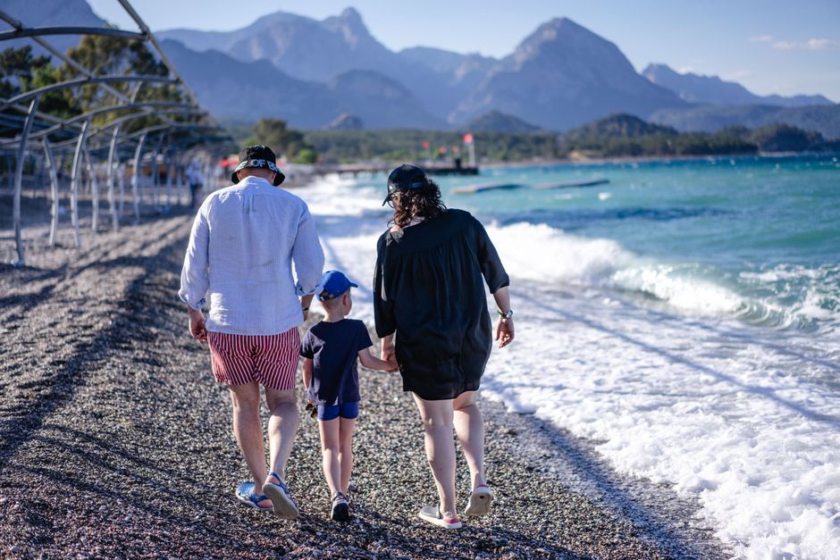 Family enjoying a sunny day at Kemer beach with mountains in the background.