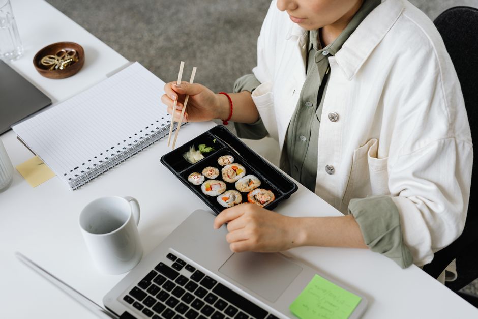 A person enjoying sushi with chopsticks at a work desk, captured from above.