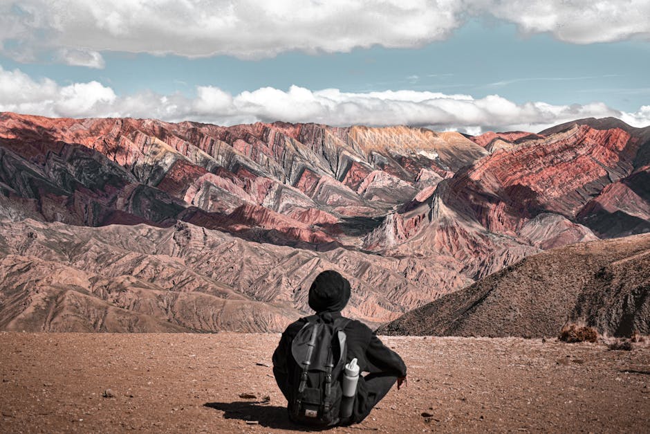 A person sitting with a backpack enjoys the view of the colorful Serranía de Hornocal mountains in Jujuy, Argentina.