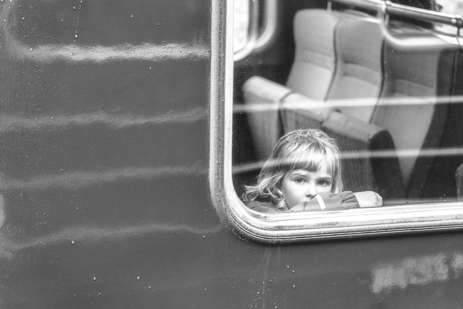A child peeks through a train window, embodying curiosity and travel in this black and white photo.