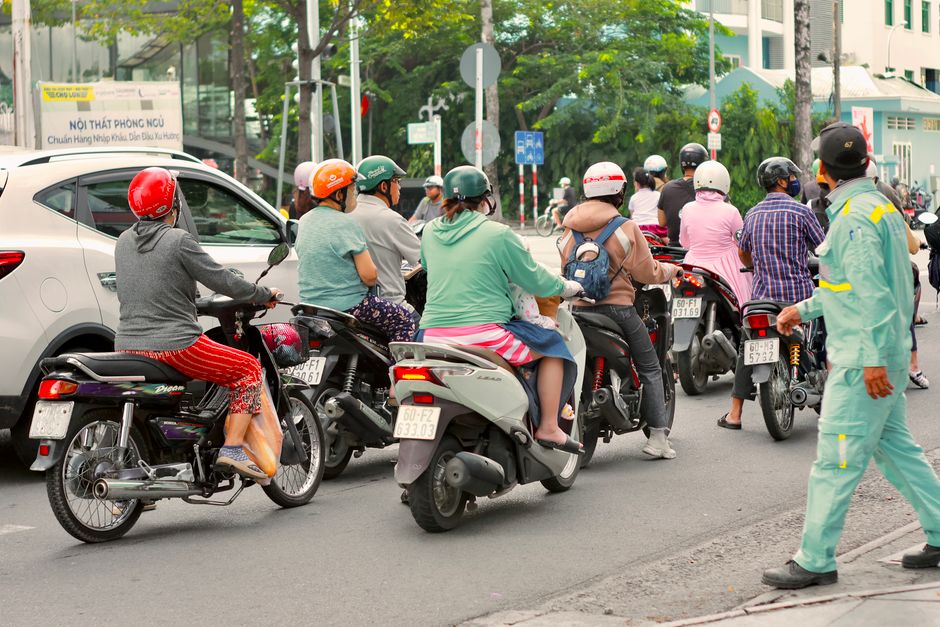 A group of people on motorbikes at an urban intersection during the day.