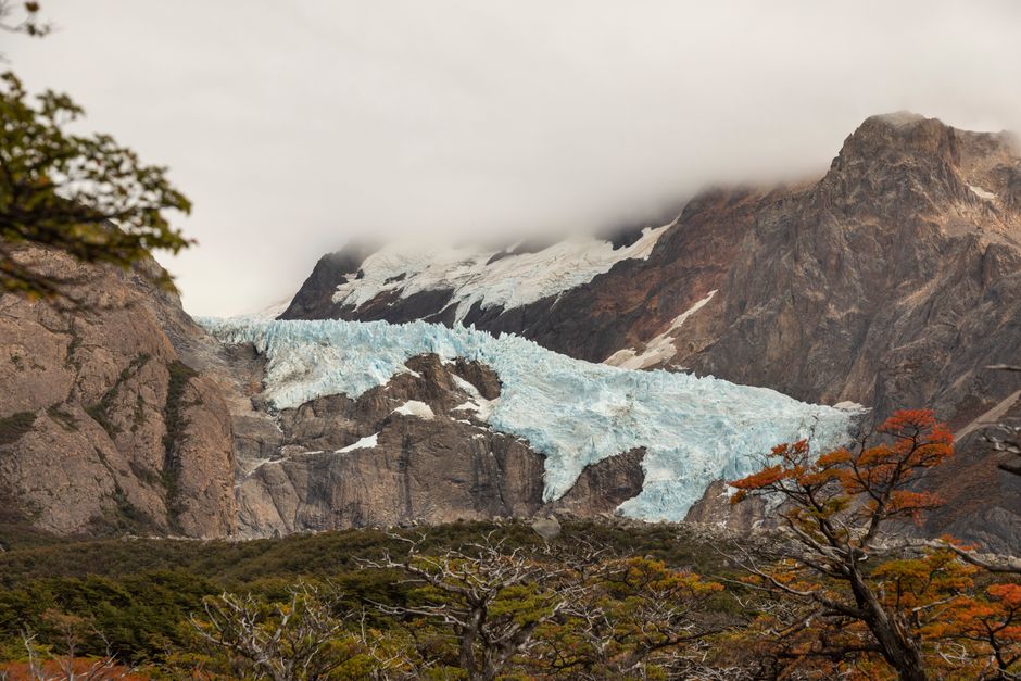 Majestic glacier flowing through rugged mountain landscape with vibrant autumn foliage.