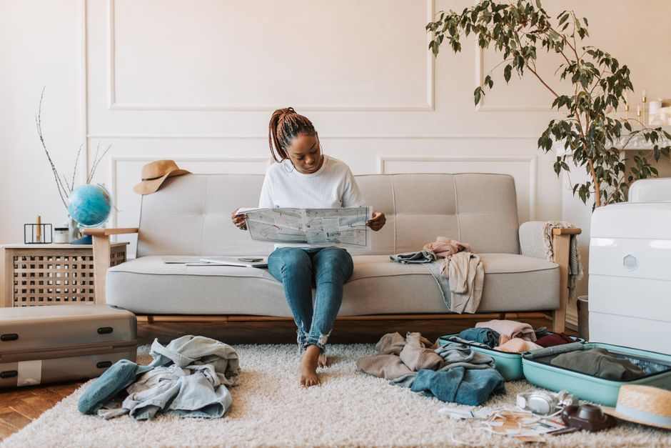 Woman preparing travel luggage with clothes on sofa